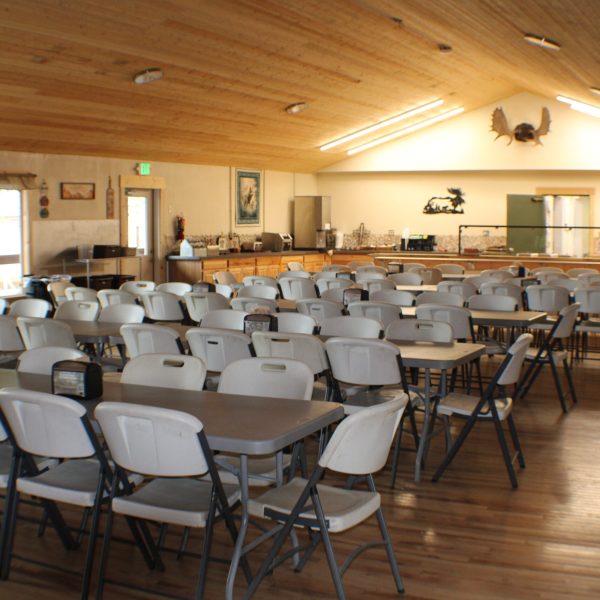 Large dining hall with vaulted wood ceiling, rows of tables and chairs, and windows facing Hourglass Lake.