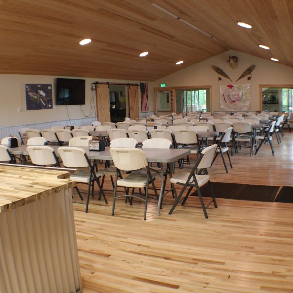 Dining hall seating with a wall mounted TV screen and barn door, snowshoes and mount displayed on the gable wall.